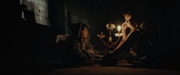 Movie still from “Tigers Are Not Afraid” (2017), directed by Issa López – Two people sitting on the ground with a lamp in a dark room; Medium shot, Over the shoulder angle