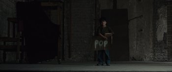 Movie still from “Tigers Are Not Afraid” (2017), directed by Issa López – A person holding a box in front of a brick wall; Wide shot, Low angle