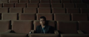 Movie still from “Tigers Are Not Afraid” (2017), directed by Issa López – A man sitting in an empty theater with his hands on the back of his chair; Wide shot, High angle