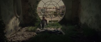 Movie still from “Tigers Are Not Afraid” (2017), directed by Issa López – A man sitting on the ground in front of a circular window; Wide shot, High angle