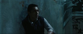 Movie still from “Tigers Are Not Afraid” (2017), directed by Issa López – A man sitting in a dark room looking off to his right; Medium shot, Low angle