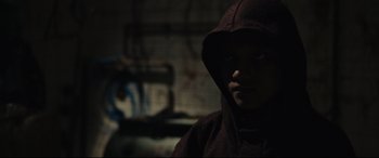 Movie still from “Tigers Are Not Afraid” (2017), directed by Issa López – A man in a hooded sweatshirt in a dark room; Close Up shot, Over the shoulder angle