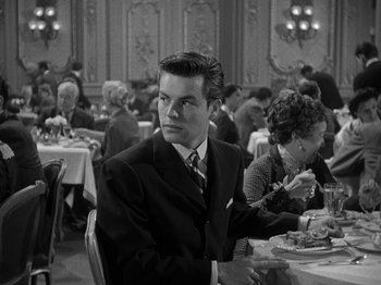 Movie still from “Titanic” (1953), directed by Jean Negulesco – A man sitting at a table in front of people; Medium shot, Over the shoulder angle
