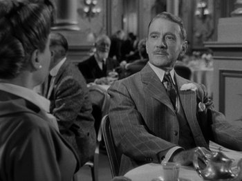 Movie still from “Titanic” (1953), directed by Jean Negulesco – A man sitting at a table with a woman in the background; Medium shot, Over the shoulder angle