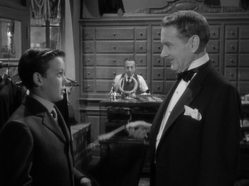 Movie still from “Titanic” (1953), directed by Jean Negulesco – A man in a suit and a bow tie talking to a boy in a suit; Medium shot, Over the shoulder angle