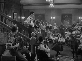 Movie still from “Titanic” (1953), directed by Jean Negulesco – A man playing an accordion in front of a crowd; Wide shot, Low angle