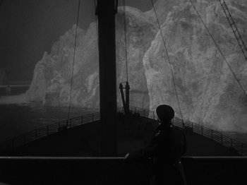 Movie still from “Titanic” (1953), directed by Jean Negulesco – A man standing on a boat looking at a large rock; Extreme Wide shot, High angle