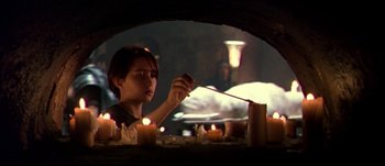 Movie still from “Titus” (1999), directed by Julie Taymor – A person lighting candles in a dark room; Medium shot, Over the shoulder angle