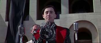 Movie still from “Titus” (1999), directed by Julie Taymor – A man in a red and black jacket standing in front of a building; Close Up shot, Low angle