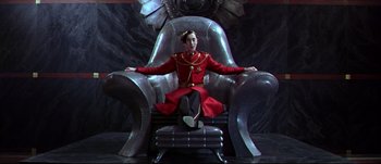 Movie still from “Titus” (1999), directed by Julie Taymor – A man in a red suit sitting on a chair; Medium shot, High angle