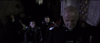 Movie still from “Titus” (1999), directed by Julie Taymor – A group of men standing next to each other in a dark room; Medium shot, Low angle
