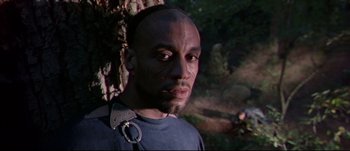Movie still from “Titus” (1999), directed by Julie Taymor – A man with a face tattoo is standing in front of a tree; Close Up shot, Low angle