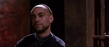 Movie still from “Titus” (1999), directed by Julie Taymor – A man with a bald head is standing in front of a wall; Close Up shot, Low angle