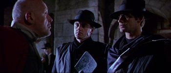 Movie still from “Titus” (1999), directed by Julie Taymor – A group of men standing next to each other wearing hats; Medium shot, Low angle