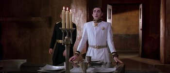 Movie still from “Titus” (1999), directed by Julie Taymor – A man in a white and black uniform standing in front of a table; Medium shot, Low angle