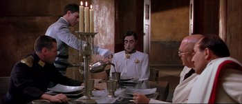 Movie still from “Titus” (1999), directed by Julie Taymor – A man sitting at a dinner table with a plate of food on the table; Medium shot, High angle