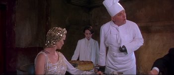 Movie still from “Titus” (1999), directed by Julie Taymor – A woman and two men in white chef's outfits preparing food in a kitchen; Medium shot, Over the shoulder angle