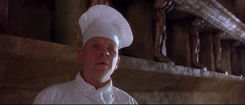 Movie still from “Titus” (1999), directed by Julie Taymor – A man wearing a chef's hat in front of a statue; Close Up shot, Low angle