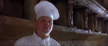 Movie still from “Titus” (1999), directed by Julie Taymor – A man wearing a chef's hat in front of a statue; Close Up shot, Low angle
