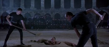 Movie still from “Titus” (1999), directed by Julie Taymor – Two men are wrestling in the sand in front of a crowd; Wide shot, High angle