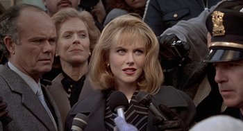 Movie still from “To Die For” (1995), directed by Gus Van Sant – A woman is holding a microphone while standing in front of a crowd; Close Up shot, Over the shoulder angle