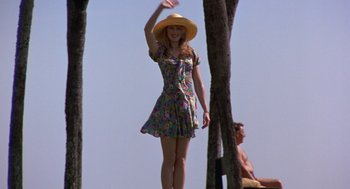 Movie still from “To Die For” (1995), directed by Gus Van Sant – A woman wearing a dress and a straw hat standing on a beach; Wide shot, Low angle