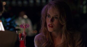 Movie still from “To Die For” (1995), directed by Gus Van Sant – A beautiful woman sitting in front of a pink flower; Close Up shot, Over the shoulder angle