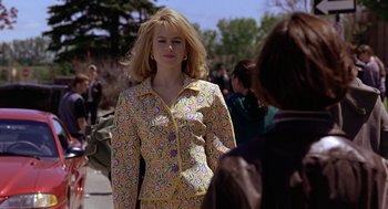 Movie still from “To Die For” (1995), directed by Gus Van Sant – A woman in a yellow and purple outfit standing next to another woman; Medium shot, Over the shoulder angle