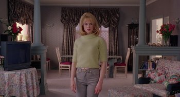 Movie still from “To Die For” (1995), directed by Gus Van Sant – A woman standing in a living room wearing a sweater; Medium shot, Low angle