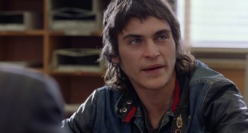 Movie still from “To Die For” (1995), directed by Gus Van Sant – A young man with long hair and blue eyes stares into the camera; Close Up shot, Over the shoulder angle