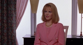 Movie still from “To Die For” (1995), directed by Gus Van Sant – A woman in a pink suit sitting in front of a lamp; Medium shot, Over the shoulder angle