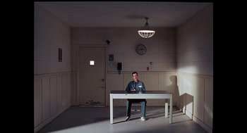 Movie still from “To Die For” (1995), directed by Gus Van Sant – A man sitting at a table in a room; Wide shot, Low angle