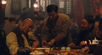 Movie still from “To Live” (1994), directed by Yimou Zhang – Two men sitting at a table with plates of food in front of them; Medium shot, Over the shoulder angle