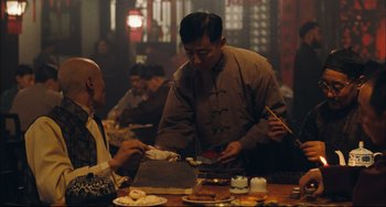 Movie still from “To Live” (1994), directed by Yimou Zhang – A man is serving food to another man; Medium shot, Over the shoulder angle