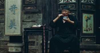 Movie still from “To Live” (1994), directed by Yimou Zhang – An old man sitting on a chair eating food; Medium shot, Over the shoulder angle