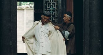 Movie still from “To Live” (1994), directed by Yimou Zhang – A man is helping another man put on a jacket; Medium shot, Low angle