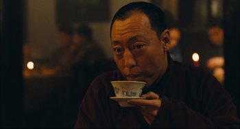 Movie still from “To Live” (1994), directed by Yimou Zhang – A man sitting at a table drinking a cup of coffee; Close Up shot, Low angle
