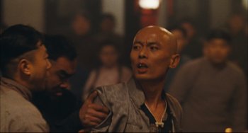 Movie still from “To Live” (1994), directed by Yimou Zhang – A man with a shaved head is standing next to a crowd of onlookers; Close Up shot, Over the shoulder angle