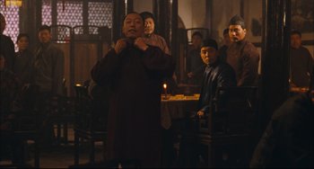 Movie still from “To Live” (1994), directed by Yimou Zhang – A group of men standing around a table; Medium shot, Over the shoulder angle