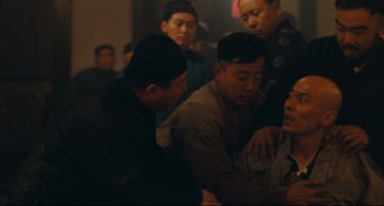 Movie still from “To Live” (1994), directed by Yimou Zhang – A group of men standing around each other in a room; Medium shot, Over the shoulder angle