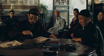 Movie still from “To Live” (1994), directed by Yimou Zhang – A group of people sitting at a table with books; Medium shot, Over the shoulder angle