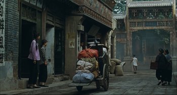 Movie still from “To Live” (1994), directed by Yimou Zhang – A man is pulling a cart full of luggage down the street; Wide shot, Low angle
