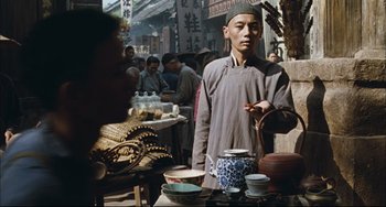 Movie still from “To Live” (1994), directed by Yimou Zhang – A man standing in front of a table with bowls and cups on top of it; Medium shot, Over the shoulder angle