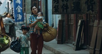 Movie still from “To Live” (1994), directed by Yimou Zhang – A woman holding a baby while walking down a street; Wide shot, Low angle
