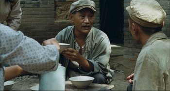 Movie still from “To Live” (1994), directed by Yimou Zhang – A man sitting at a table with a cup of tea; Medium shot, Over the shoulder angle