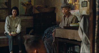Movie still from “To Live” (1994), directed by Yimou Zhang – A man sitting at a table with a plate of food; Medium shot, Over the shoulder angle