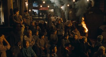 Movie still from “To Live” (1994), directed by Yimou Zhang – A group of people sitting in a room with smoke coming out of a chimney; Wide shot, High angle