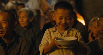 Movie still from “To Live” (1994), directed by Yimou Zhang – A young boy holding a bowl in his hands; Medium shot, Over the shoulder angle