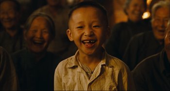 Movie still from “To Live” (1994), directed by Yimou Zhang – A young boy smiling for the camera with a group of people in the background; Close Up shot, High angle
