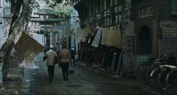 Movie still from “To Live” (1994), directed by Yimou Zhang – Two people walking down a street near a building; Wide shot, High angle